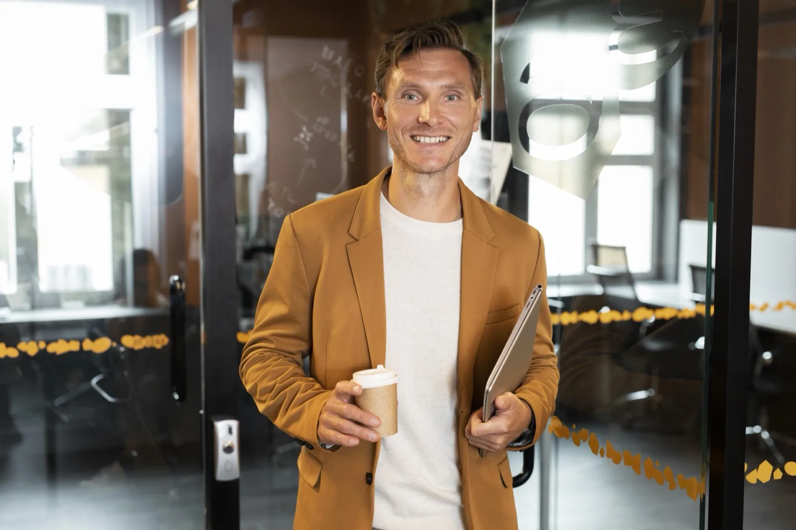 Confident professional at office doorway with coffee and laptop